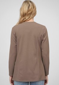 Veste longue à manches longues de couleur marron avec un col arrondi et un ourlet légèrement évasé, présentant un design de dos lisse et sans poches visibles.