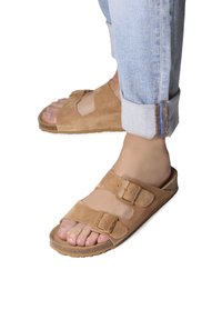 Sandales en daim beige avec deux boucles ajustables, semelle intérieure anatomique et semelle texturée. Portées avec un jean en denim clair retroussé.