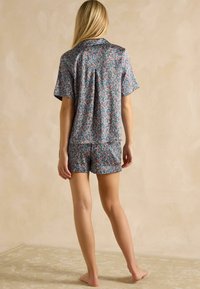 Kvetinový pyžamo set s krátkymi rukávmi v modrom vyhotovení, s živou potlačou a jemnou tkaninou. Voľný strih s golierom a jednofarebnými šortkami.