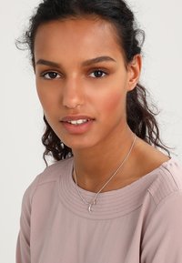 Sølvpandant halskæde med halvmåne- og stjernecharms, båret af en model med lysebrunt hår og en lys pink tekstureret bluse.