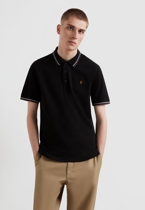 Zwarte polo met contrasterende witte kraag en mouwafwerking, voorzien van een klein oranje logo op de borst. Glad, textuurstof.