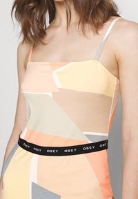 Kolorowa dopasowana koszulka na ramiączkach z miękkiej mieszanki bawełny, z geometrycznymi wzorami w kolorach brzoskwiniowym, beżowym i szarym. Czarny detal z logo w pasie.