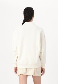 Sudadera de gran tamaño en color crema con hombros caídos, puños de canalé y dobladillo. La parte posterior presenta una pequeña etiqueta en el cuello.