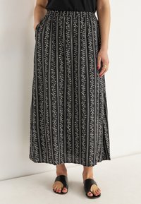 Schwarzer Maxirock mit weißem Blumenmuster und vertikalen Streifen, ausgestattet mit einem elastischen Taillenbund und Seitentaschen. Kombiniert mit schwarzen Riemensandalen.