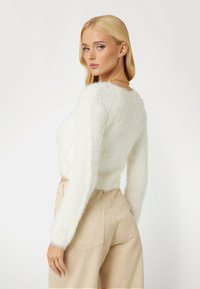 Witte, donzige cropped trui met lange mouwen, ronde halslijn, gecombineerd met beige, high-waisted broek met achterzakken en een aansluitende silhouet.