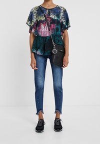 Top a maniche corte con fantasia floreale multicolore, abbinato a jeans skinny blu strappati e sneakers nere, accessoriato con una borsa a tracolla nera.