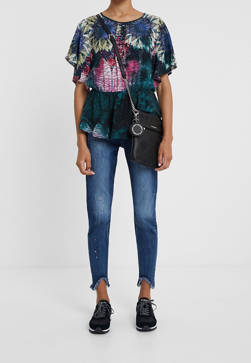 Top a maniche corte con fantasia floreale multicolore, abbinato a jeans skinny blu strappati e sneakers nere, accessoriato con una borsa a tracolla nera.