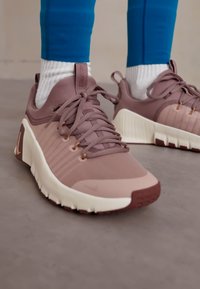 Nike sportcipők világos mályva színben, texturált felsőrész, rózsaszín kiegészítők és fehér talp hullámmintával és kiemelkedő logóval.