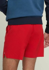 Bañador rojo con bolsillos laterales, hecho de una tela suave. Presenta un dobladillo abierto con un pequeño acento blanco, combinado con una parte superior azul marino.