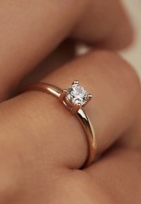 Roségoldring mit einem glatten Band und einem auffälligen runden, klaren Stein, der sicher von vier Krappen gehalten wird, an einer Hand.