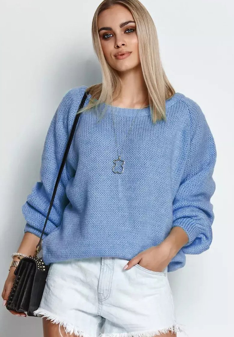Błękitny sweter z dzianiny o szerokim dekolcie i luźnym kroju, zestawiony z białymi szortami dżinsowymi. Widać czarną torebkę i srebrną bransoletkę.