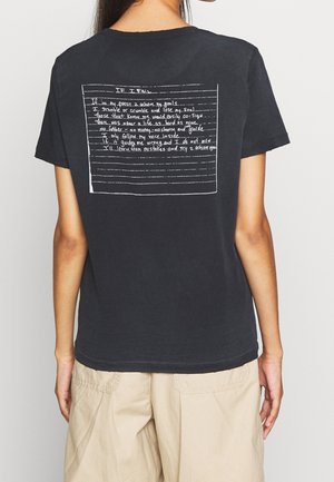 Czarna bawełniana koszulka o luźnym kroju. Na plecach znajduje się biały nadruk z tekstem w ramce z liniami, utrzymany w stylu odręcznego pisma.