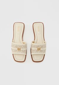 Sandalias tipo slide beige con una correa texturizada que presenta un patrón de logotipo y detalle de hardware dorado. Plantilla lisa y suela exterior de goma marrón.