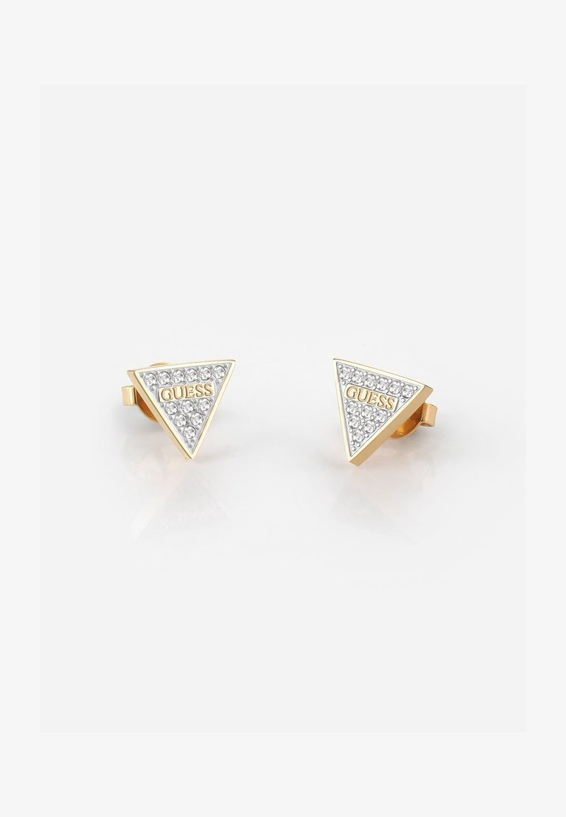 Boucles d'oreilles clous triangulaires ton or avec des cristaux transparents et le logo "GUESS" au centre sur fond blanc.