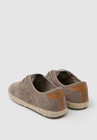 Espadrilles de ante gris con suela de yute trenzado, adornadas con detalles de cuero marrón y punta redondeada. Dos ojales para los cordones en la parte delantera.