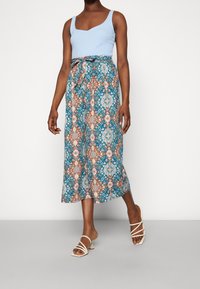 Top sans manches bleu associé à des culottes à motifs avec des motifs floraux turquoise, orange et blancs. Les culottes possèdent une taille à nouer.
