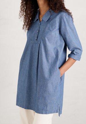 Denim-mekko vaaleansinisessä värissä, jossa on kauluspääntie, nappilista, 3/4-hihat ja sivutaskut laskostetulla yksityiskohdalla.