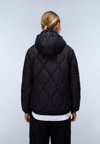 Svart vadderad pufferjacka med huva, med en mjuk textur och rundad mönstring. Ärmarna har elastiska detaljer för en tät passform.