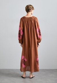 Braunes Maxikleid mit langen Ballonärmeln, ausgestattet mit pinkfarbenem Blumenstickerei an den Ärmeln. Geraffter Halsausschnitt, leichtes Material, knöchellang.