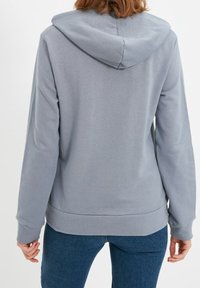Sudadera con capucha en gris claro, hecha de tela suave. Cuenta con mangas largas, un corte holgado, y puños y dobladillo acanalados.