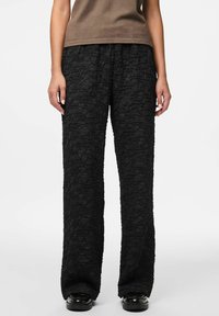Zwarte gestructureerde wide-leg broek met een gekreukt patroon, zachte stof en een elastische tailleband voor comfort. Gecombineerd met een bruine top.