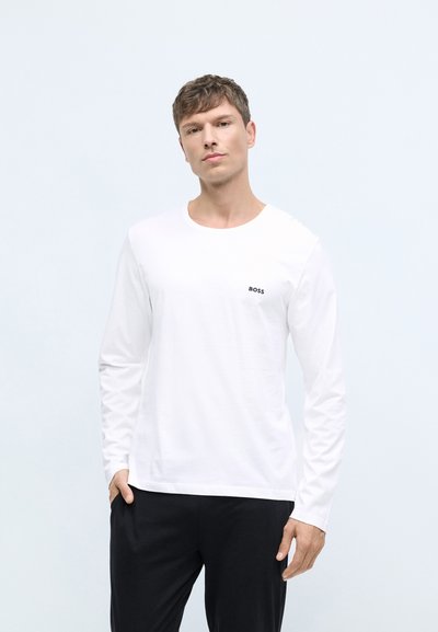 Chemise blanche à manches longues avec col rond, arborant un petit logo noir "BOSS" sur la poitrine gauche et une texture en coton lisse.