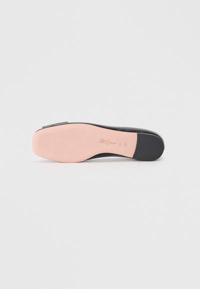 Chaussure plate noire avec une tige en cuir lisse, bout arrondi et semelle rose texturée, arborant un logo en relief et des détails de design minimalistes.