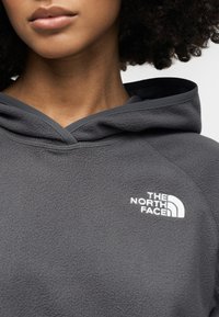 Γκρι fleece φούτερ με κουκούλα και κορδόνι, υφή υφάσματος, και λευκό λογότυπο στο στήθος. Διαθέτει κυρτό στρίφωμα  και ελάχιστες ραφές.