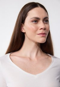 White V-neck shirt made of soft fabric, featuring a smooth texture and minimal stitching. Model with long, straight brown hair and clear skin.