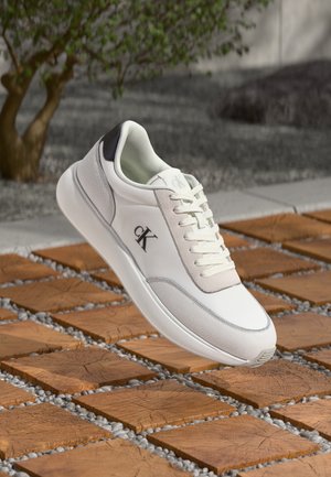 White leather sneaker with a grey accent and logo on the side. Features round toe, lace-up design, and textured side panels.