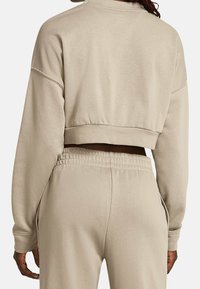 Beige zkrácená mikina s širokými rukávy, hladkým materiálem a elastickým lemem. Spojená s odpovídajícími kalhotami s elastickým páskem.