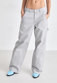 Pantalones de pierna ancha de color gris claro, confeccionados en algodón, con bolsillos laterales y cintura alta, combinados con zapatos de tacón azul.