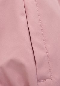 Rosa tyg med en mjuk, slät textur, med framträdande sömmar och en lätt glans, som visar en vikning och en sidoseamsdetalj.