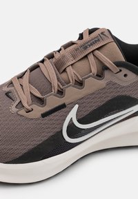 Braune Mesh-Sneaker mit einem schwarz-weißen Swoosh-Design, strukturierten Akzenten und beigen Schnürsenkeln. Verfügt über eine geschwungene Silhouette und eine Gummisohle.