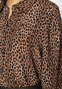 Blusa con stampa leopardata in tessuto morbido, con scollatura con colletto e chiusura con bottoni neri, che presenta motivi marroni e neri.