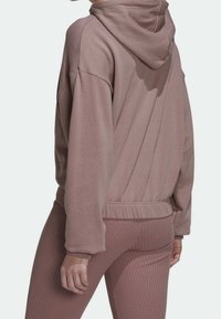 Sweat-shirt rose poussiéreux à capuche, poignets et ourlet côtelés ; tissu doux et texturé ; porté avec des leggings côtelés assortis. Vue de dos.