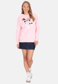 Sudadera rosa claro con diseños bordados juguetones de animales; combinada con una minifalda vaquera y zapatillas blancas con detalles coloridos.