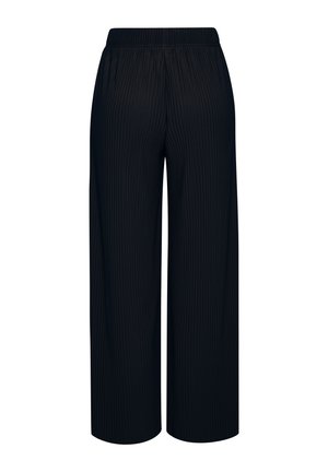 Close-up van een persoon die zwarte geplooide broek draagt met een elastische tailleband en een hand die naast het dijbeen rust.