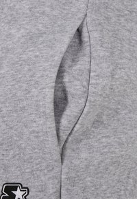 Grijze sweatshirt van een geweven stof, met een zakdetail aan de zijkant en een contrasterend geborduurd logo in zwart.