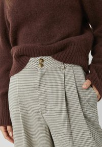 Pull bordeaux en matière douce, associé à un pantalon taille haute à carreaux avec des plis et deux boutons bruns visibles à la ceinture.