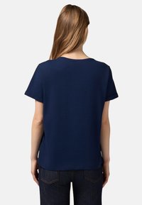 Camiseta de manga corta azul marino con cuello redondo, puños enrollados y un corte relajado. La tela parece suave y lisita.