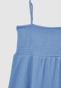 Robe en tissu bleu texturé avec corsage smocké et fines bretelles sur un fond clair uni.
