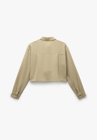 Kraftigt beige skjorte med lange ærmer, knaplukning ved håndleddene og krave. Har to baglommer og en glat tekstur.