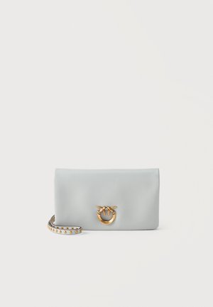 Pochette en cuir gris clair avec une fermeture en forme d’oiseau doré et un bracelet assorti orné de clous dorés, sur un fond uni.