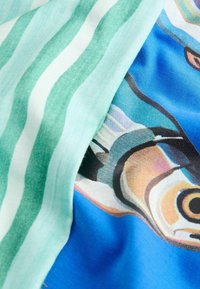 Gros plan sur un tissu à rayures vertes et blanches à côté de poissons imprimés colorés sur fond bleu.