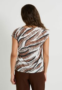 Top de manga corta en tejido ligero con un atrevido patrón de rayas de animales en tonos marrón y negro sobre un fondo claro. Cuello circular.