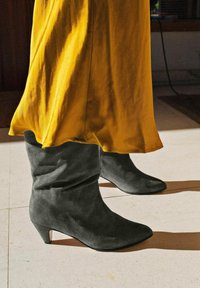 Schwarze Wildlederstiefeletten mit einem lässigen Design, spitzer Zehenpartie und kleinem Absatz, kombiniert mit einem fließenden gelben Rock.