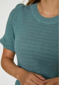 Strickpullover in Teal mit kurzen Puffärmeln, geripptem Rundhalsausschnitt und einem strukturierten offenen Muster. Liegt eng am Körper an.