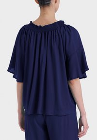 Blusa blu navy con scollo smock, maniche corte a volant e vestibilità ampia. Realizzata in tessuto leggero e fluido.