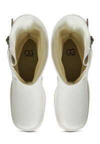 Białe gumowe buty z gładką fakturą, zaokrąglonym noskiem i minimalistycznym designem. Wnętrze ma jasną podszewkę z logo na dole.